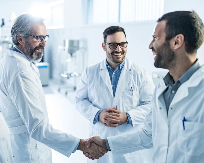 three scientists in lab coats shaking hands