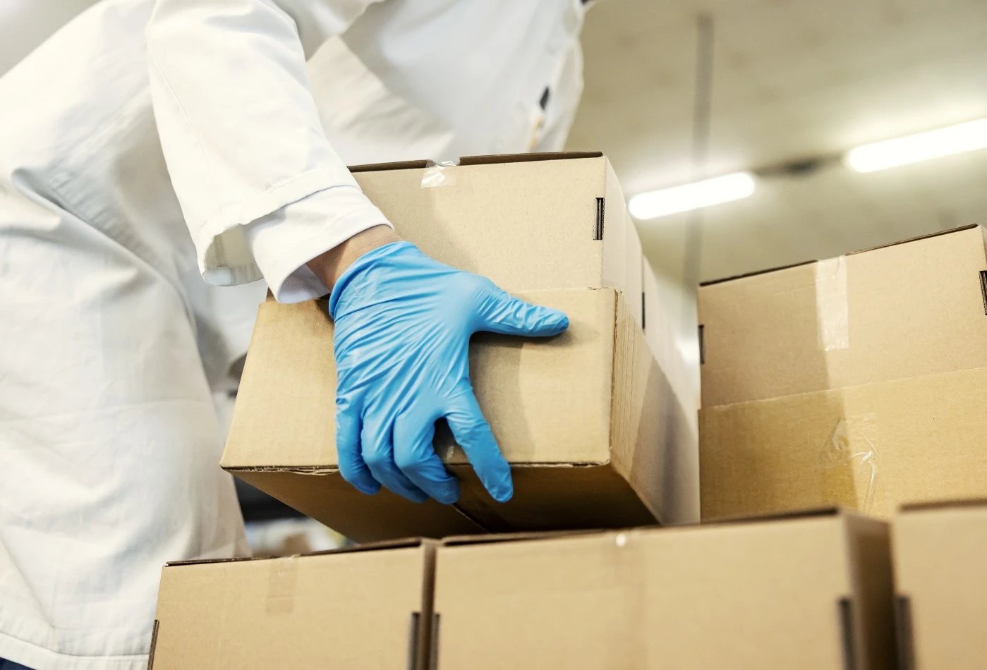 Plain brown box being picked up by woman wearing blue gloves and white lab coat