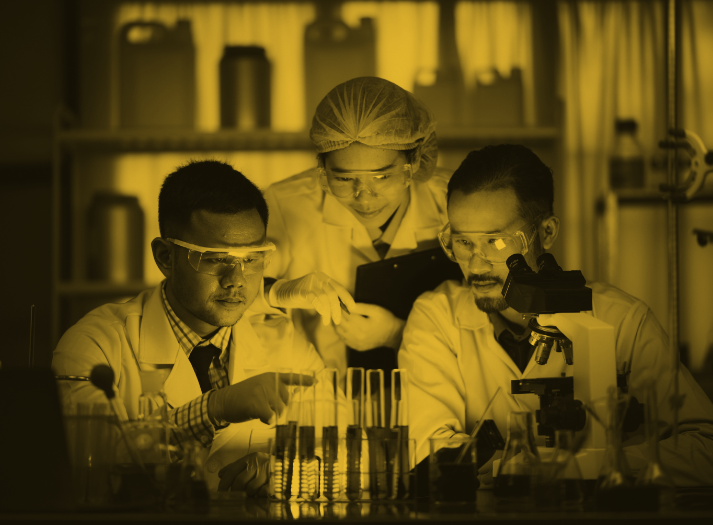 3 scientists wearing lab gear looking at lab equipment