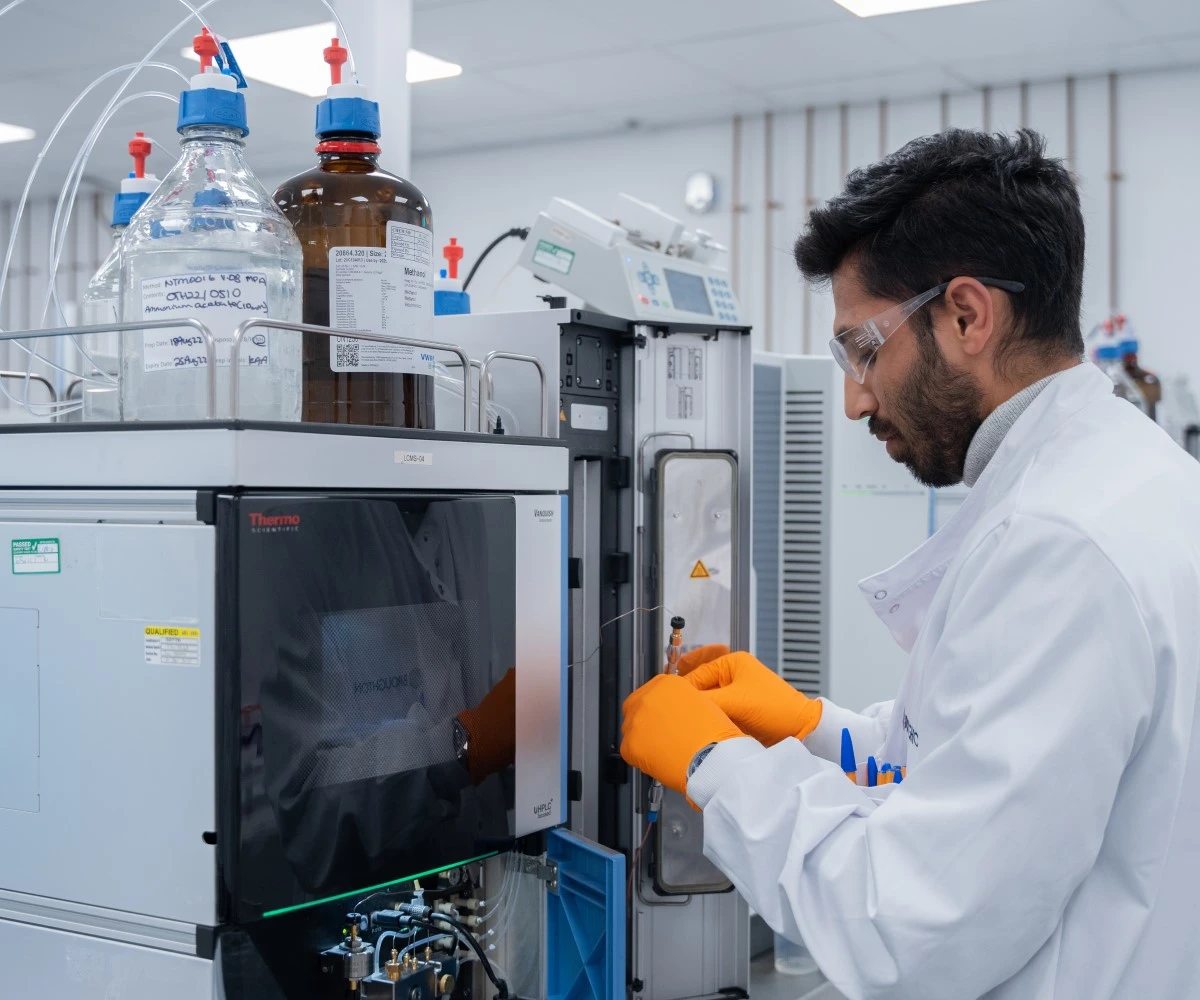 Broughton male scientist wearing orange gloves, goggles and lab coat testing nicotine products